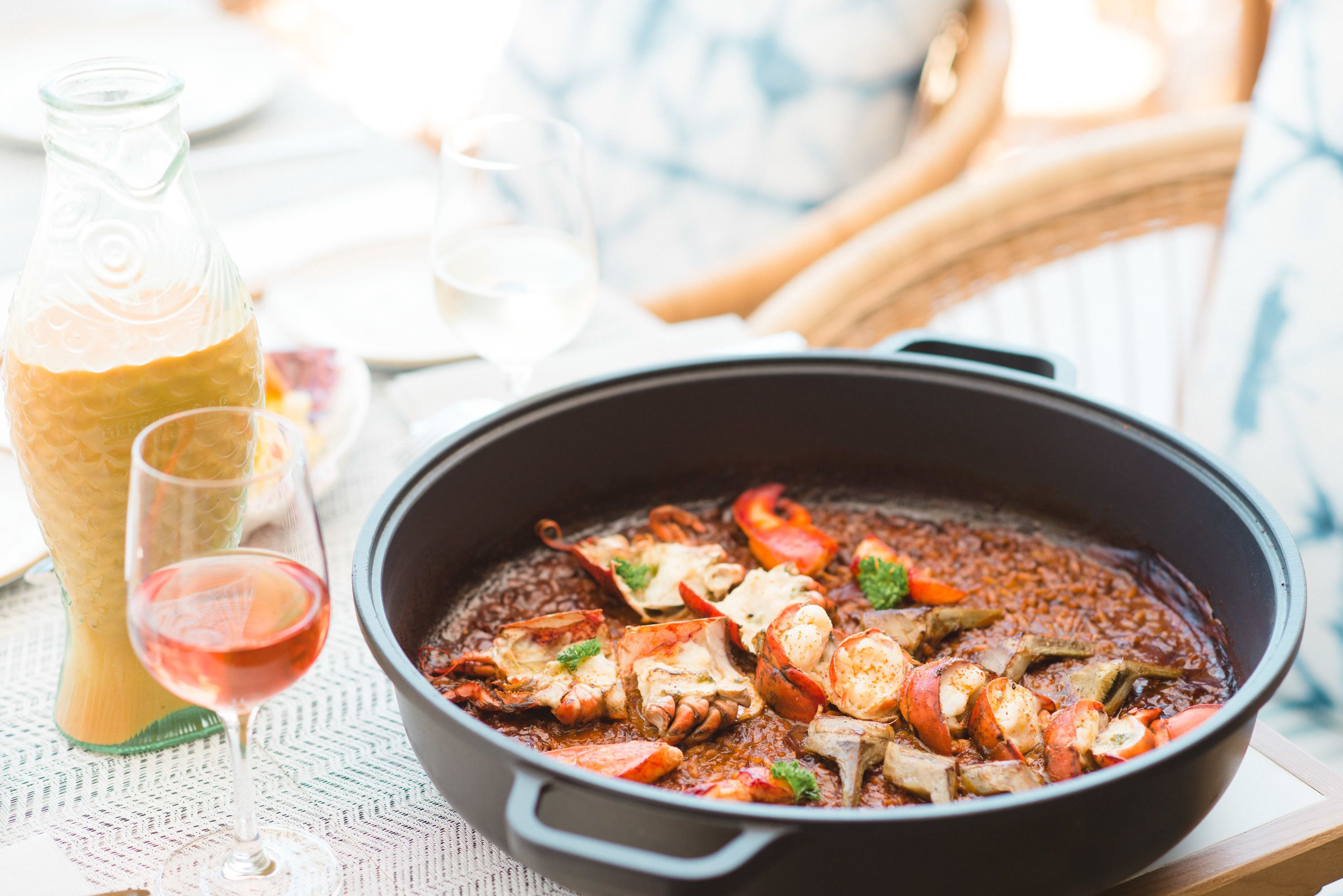 Una olla grande de guiso de mariscos con una botella y vasos sobre una mesa.