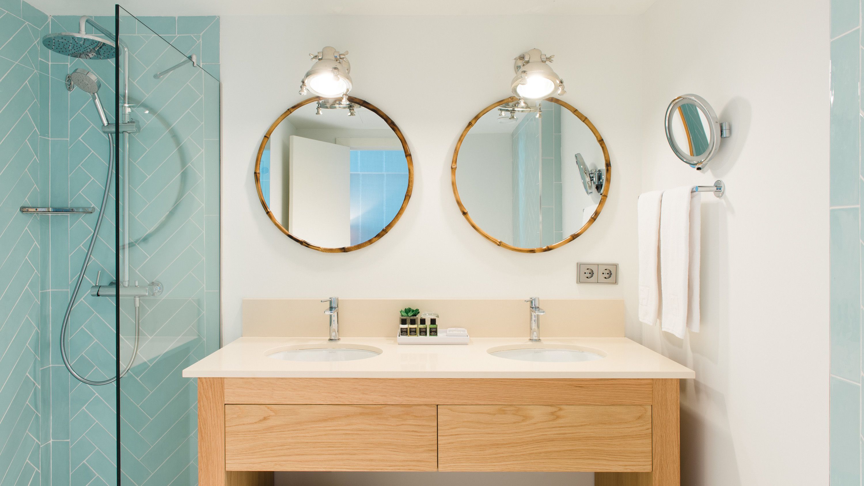 A bathroom with two sinks, a glass shower enclosure, and two round mirrors with lights.