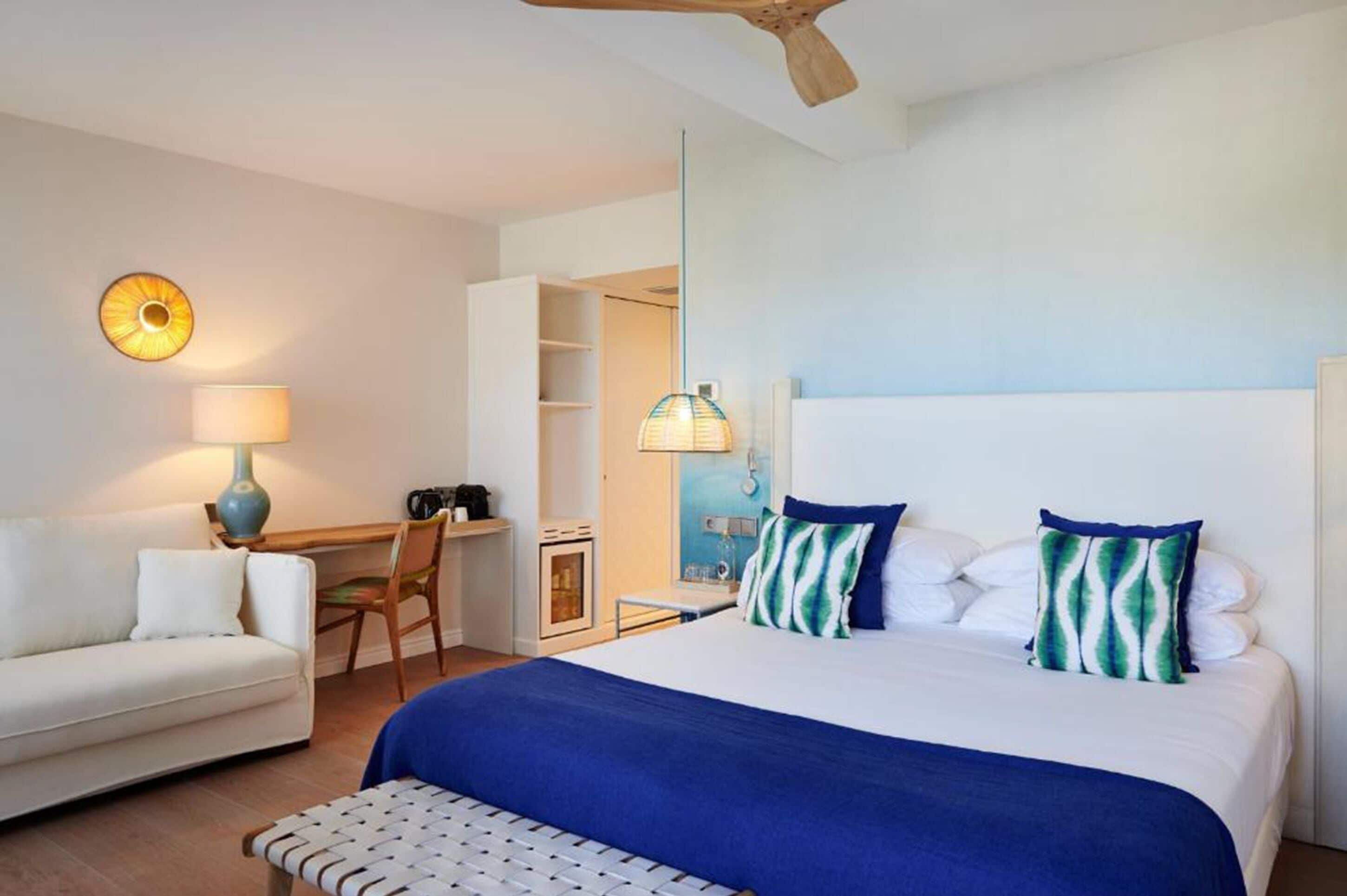 Una habitación de hotel con cama, escritorio, silla, sofá y ventilador de techo.