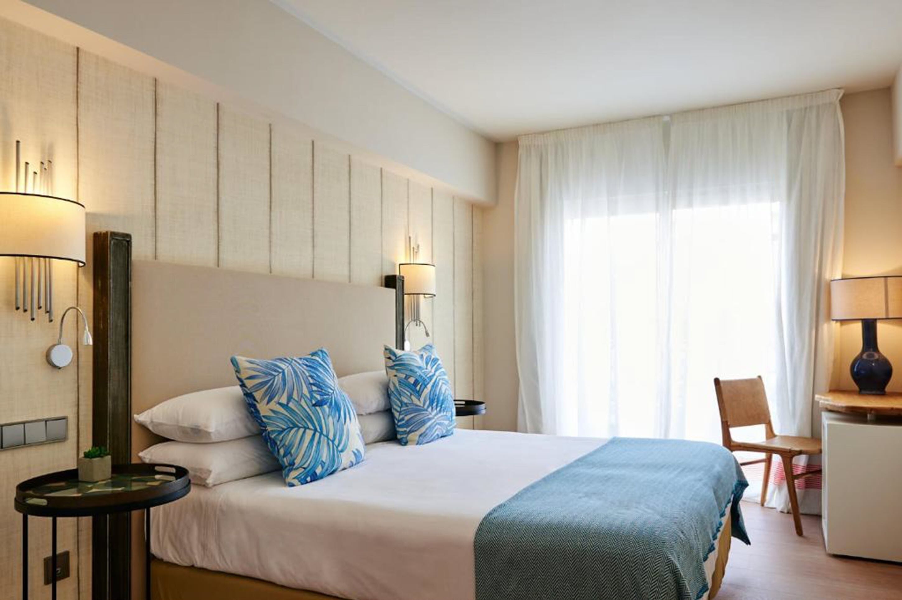 A hotel room with a bed, bedside lamps, a desk, and a chair.