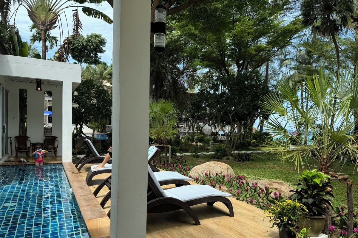 A pool area with lounge chairs, a child playing, and a garden with various plants and a large rock.