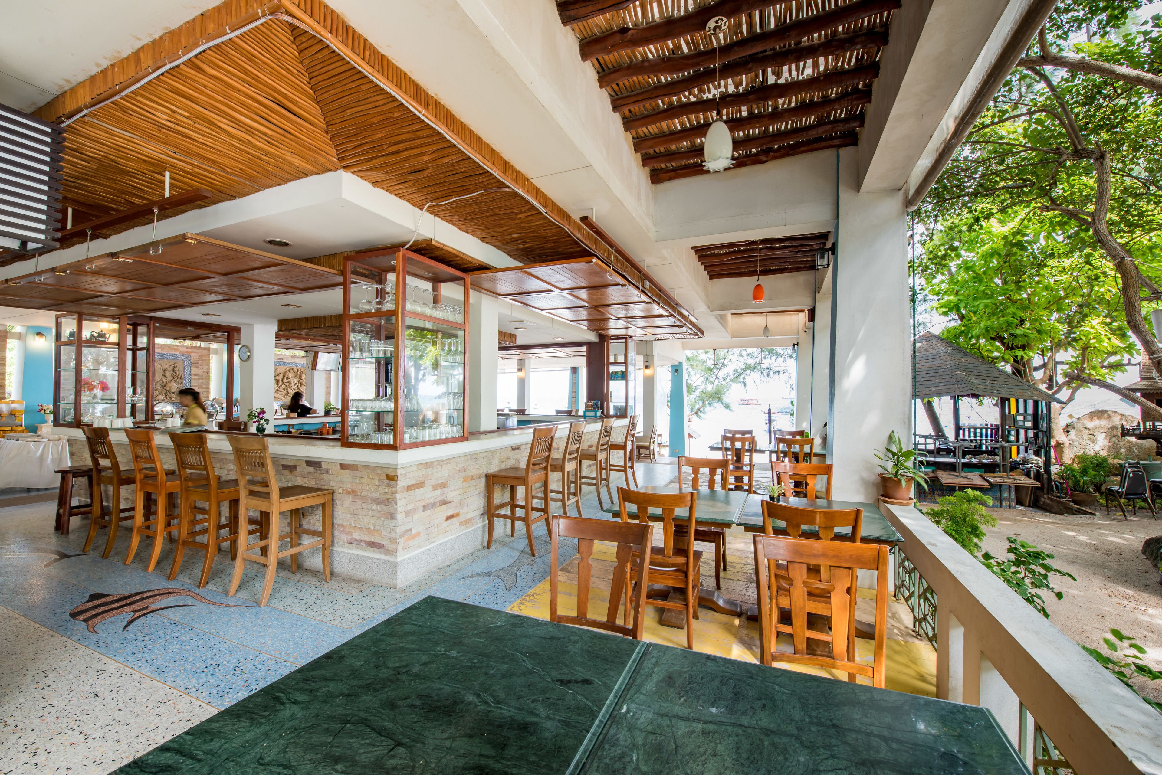 Ein Restaurant mit Holztischen, einer Bar und Blick ins Freie.