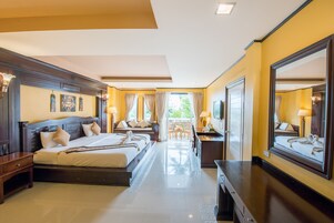 A hotel room with a large bed, a desk, a chair, and a balcony with a view of greenery.