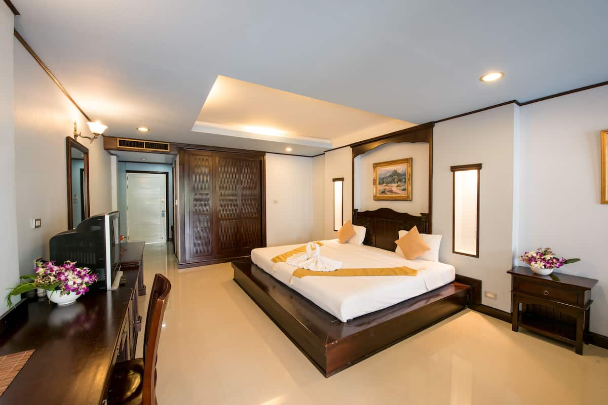 A hotel room with a large bed, a desk with a chair, a small table with flowers, and a painting on the wall.