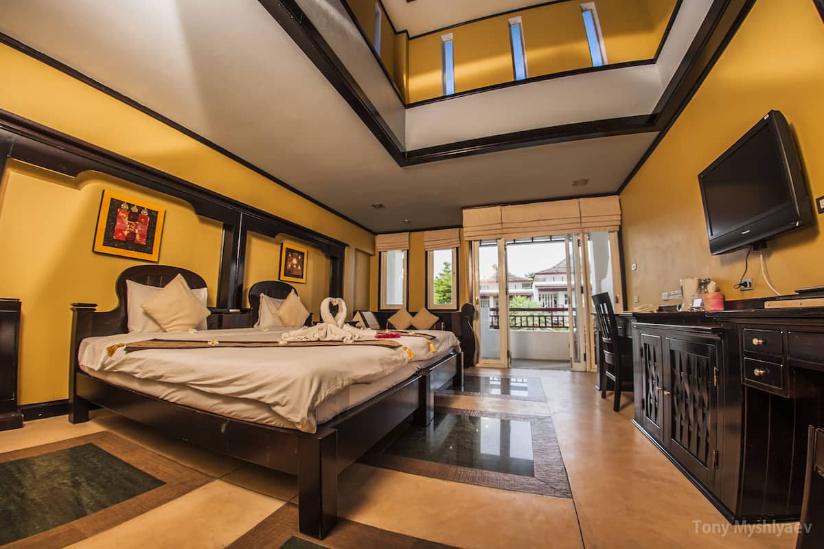 A hotel room with a large bed, a television, a desk, and a balcony with a view.