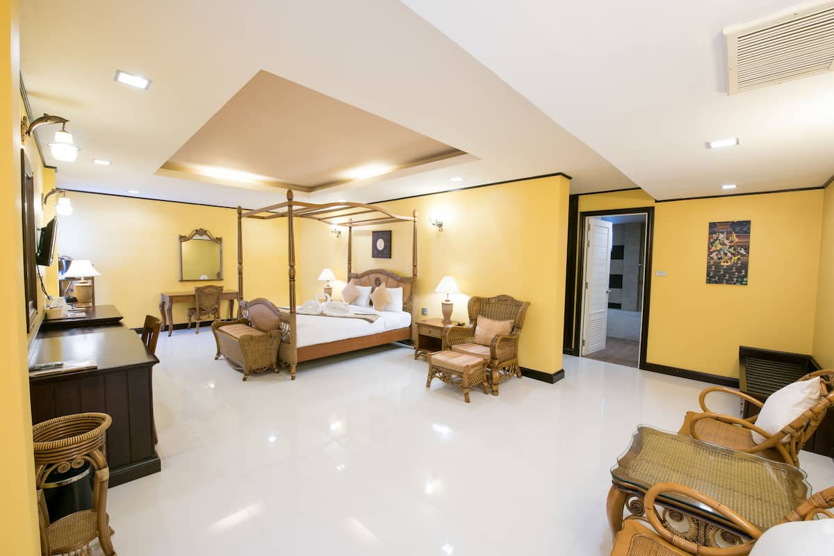A spacious hotel room with a four-poster bed, a desk with a chair, and two wicker chairs.
