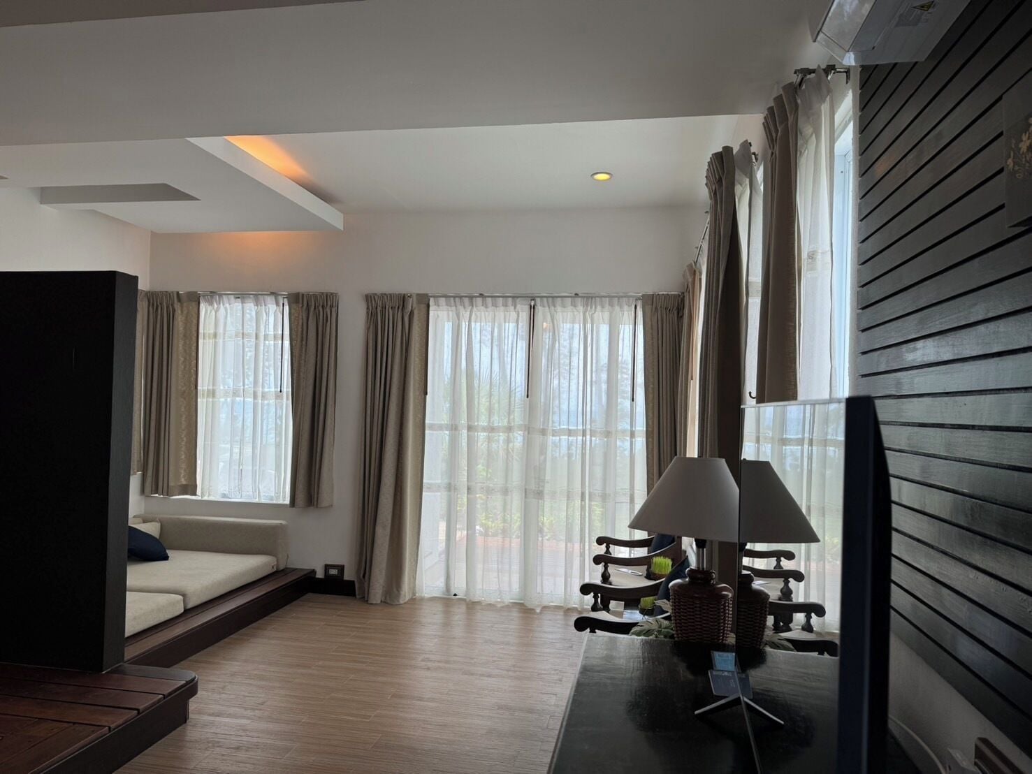 Un salon moderne avec un canapé, une lampe et une vue sur l’extérieur grâce à de grandes fenêtres.