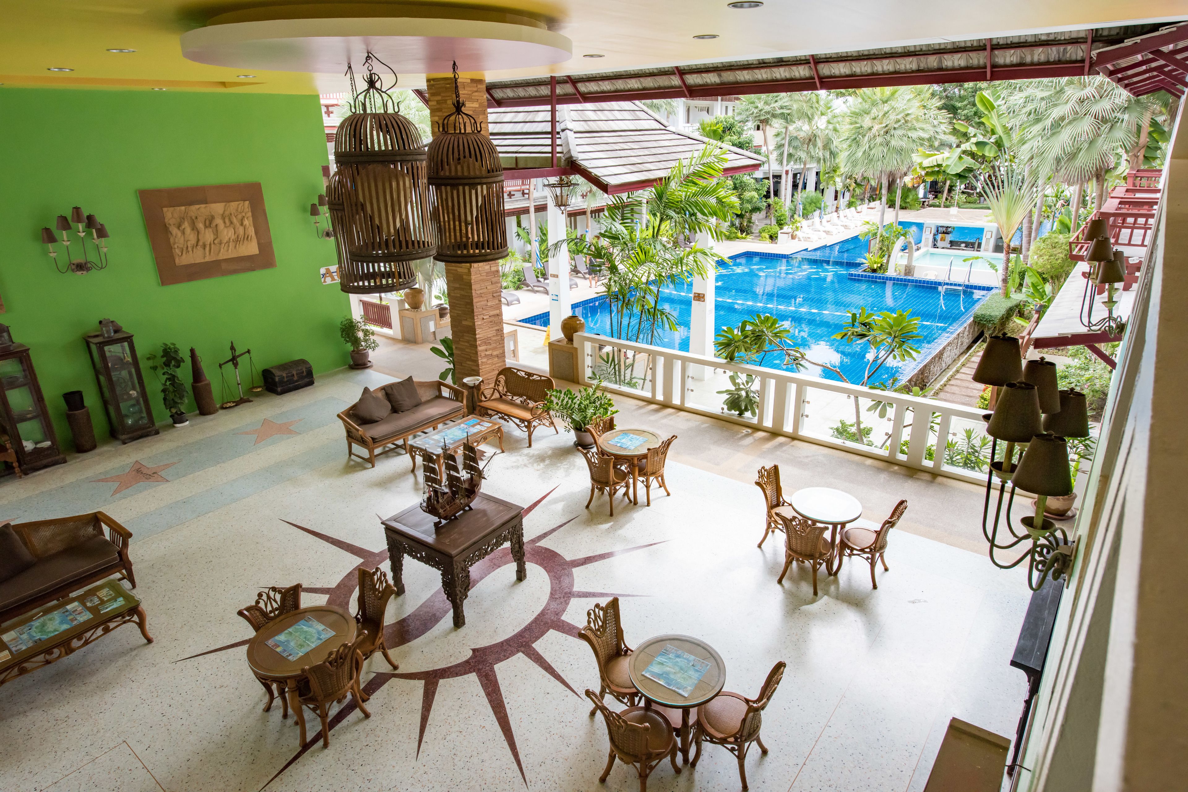 A hotel lobby with a pool view, featuring wicker furniture, a star-shaped floor design, and a green wall with artwork.