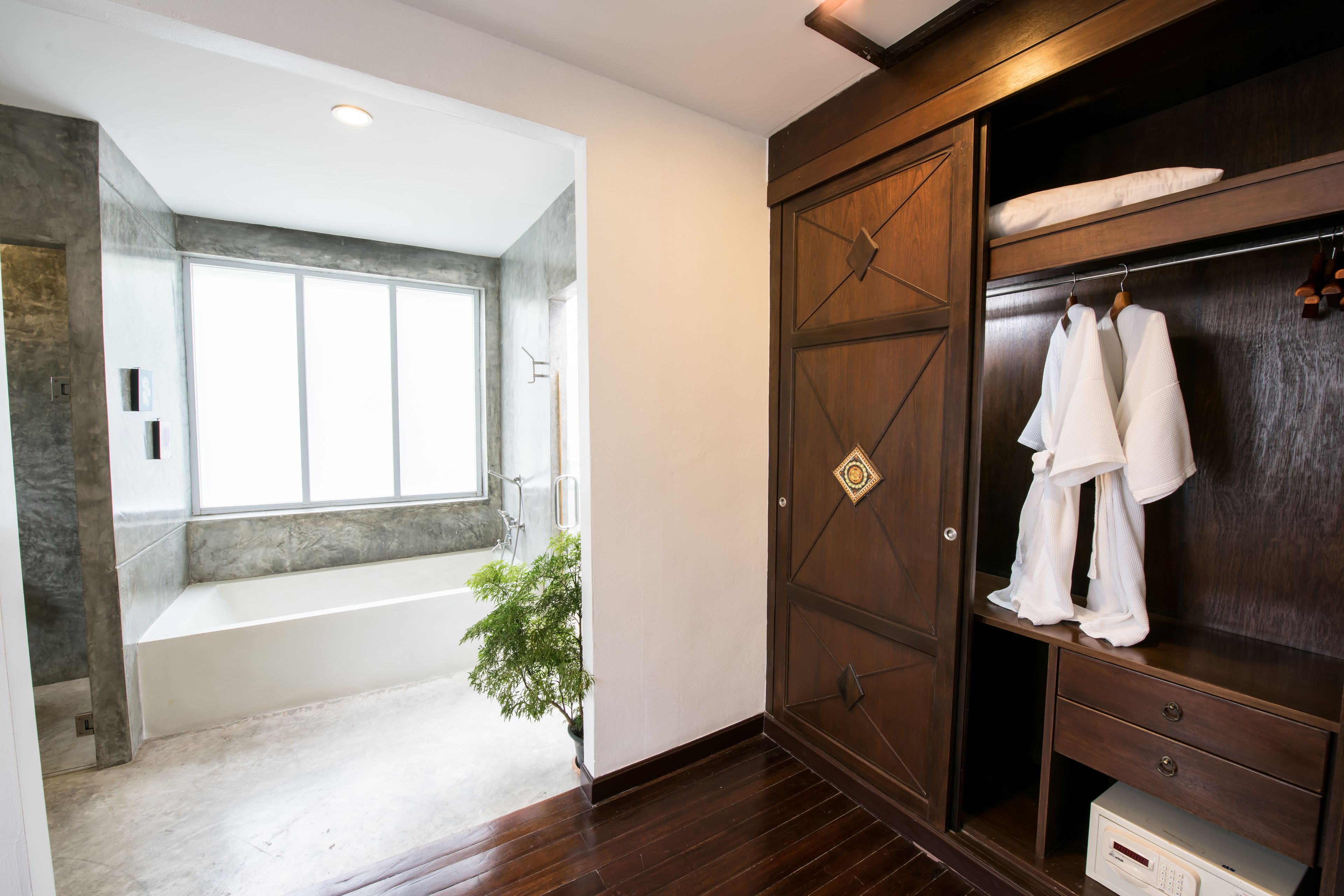 Un baño moderno con un ventanal grande, una bañera y un armario de madera con albornoces colgados.