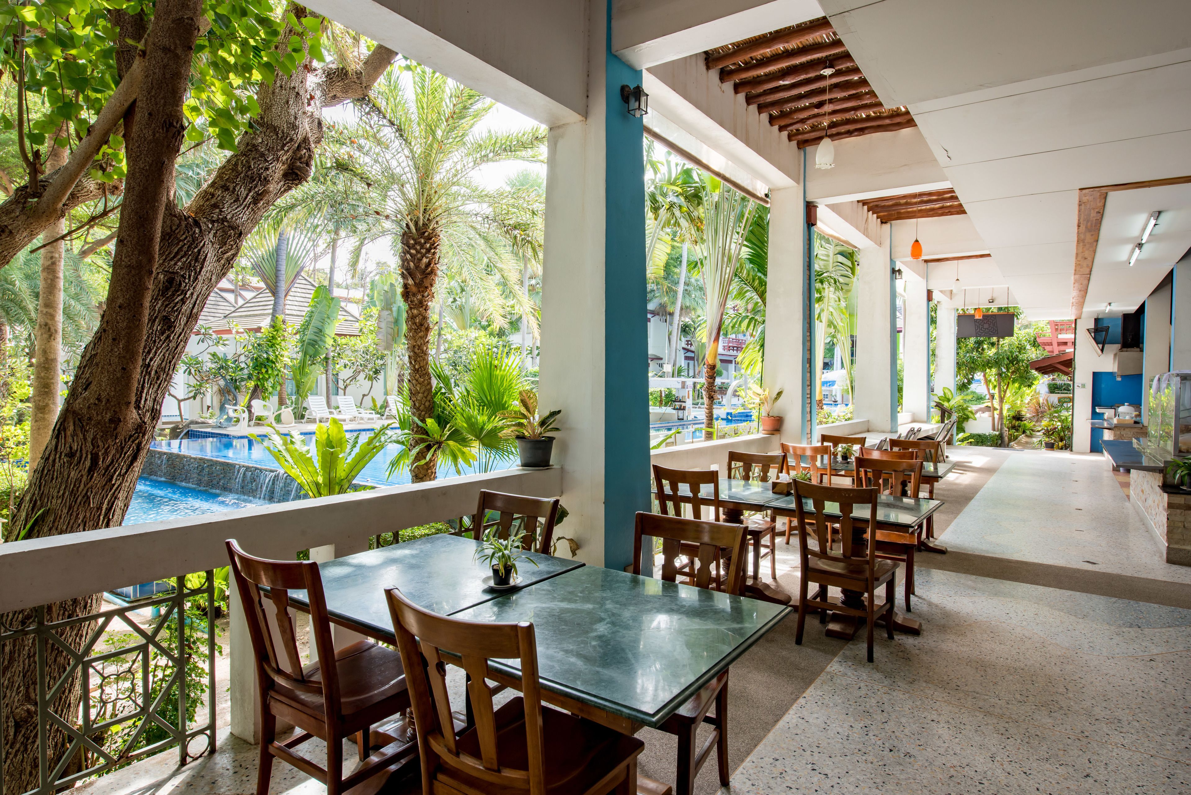 A restaurant with outdoor seating, a pool, and tropical plants.