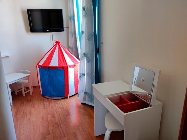 A room with a small white desk, a red and blue tent, a television mounted on the wall, and a window with curtains. - eó Gran Canaria Aeropuerto - Business and Events (Santa Lucia)