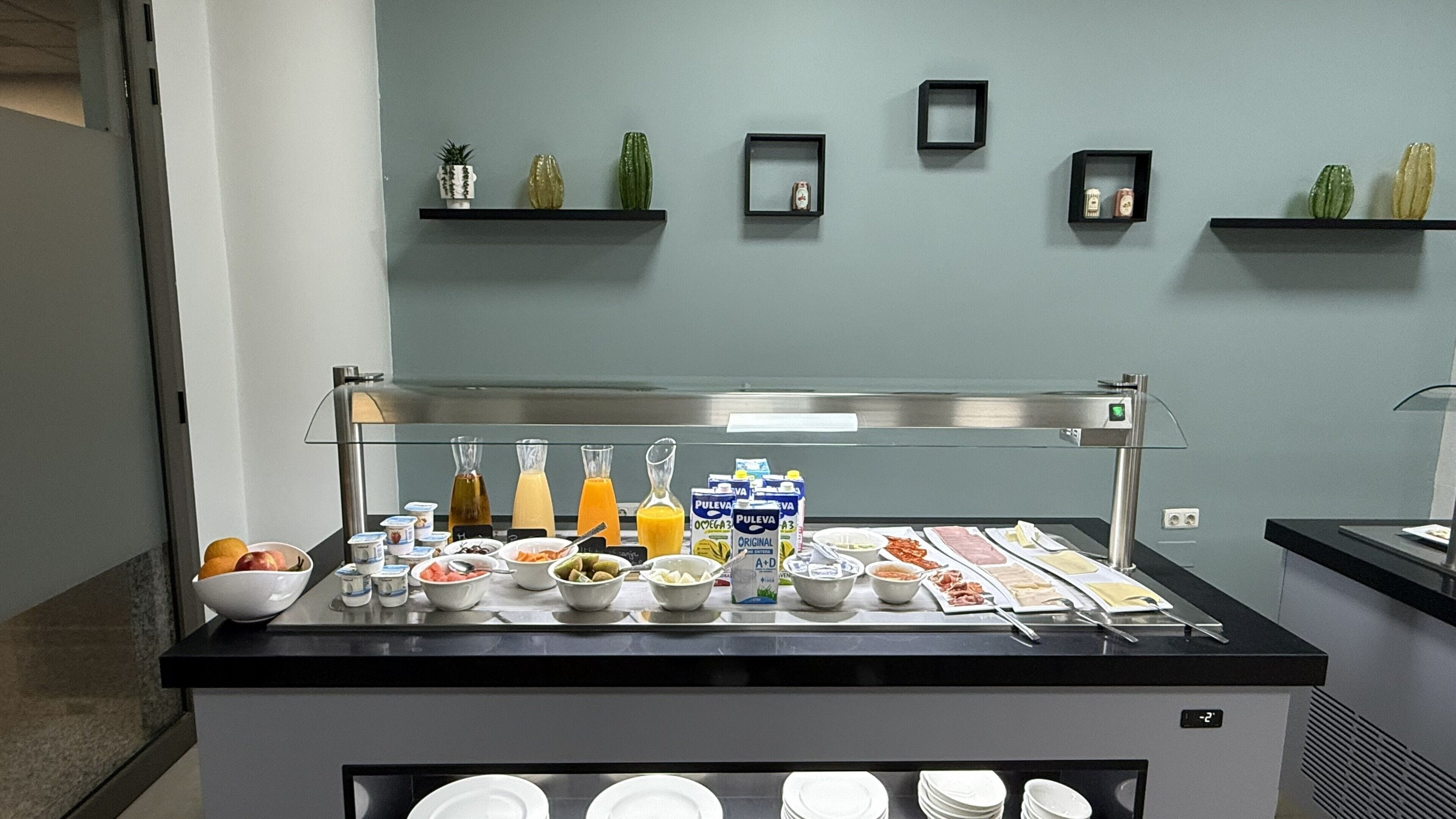 Montaje tipo bufé con diversos alimentos y bebidas, una máquina de café y un refrigerador.