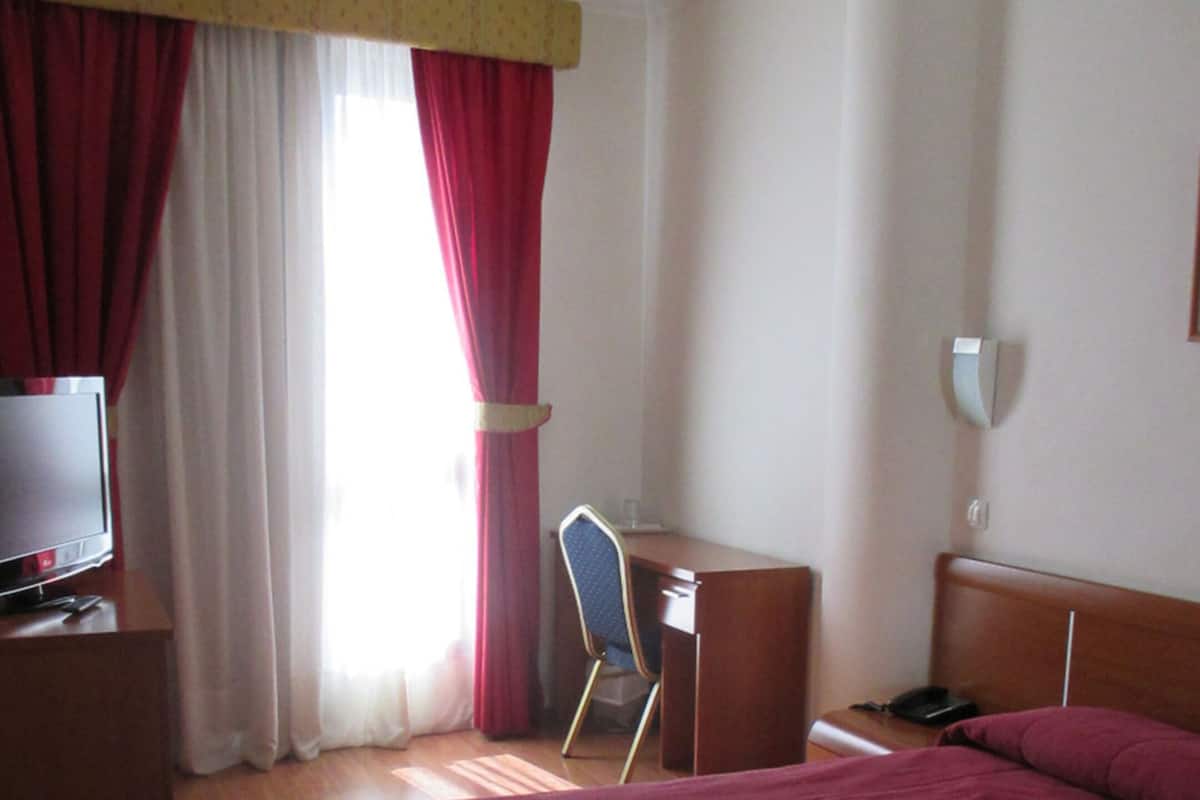 Ein Hotelzimmer mit einem Bett, einem Schreibtisch, einem Stuhl, einem Fernseher und einem Telefon.