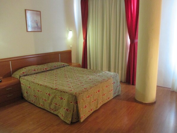 A bedroom with a wooden bed, a nightstand, a wall-mounted lamp, and a window with red curtains. - eó Gran Canaria Aeropuerto - Business and Events (Santa Lucia)
