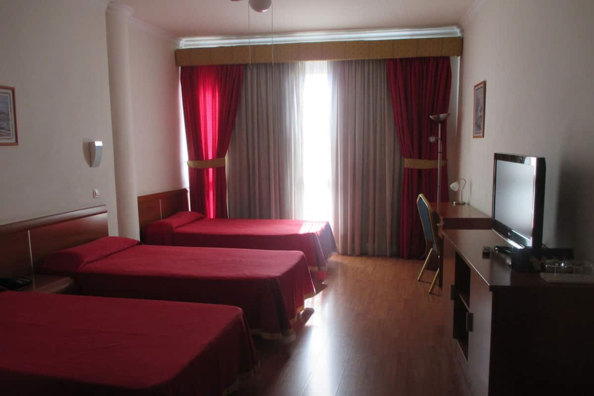 Ein Hotelzimmer mit zwei Einzelbetten, einem Schreibtisch mit Fernseher und einem Fenster mit roten Vorhängen.
