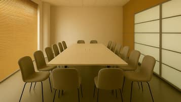 Una sala de conferencias con una mesa larga y varias sillas, una ventana con persianas y una pared con un diseño de cuadrícula.