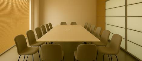 Una sala de conferencias con una mesa larga y varias sillas, una ventana con persianas y una pared con un diseño de cuadrícula.