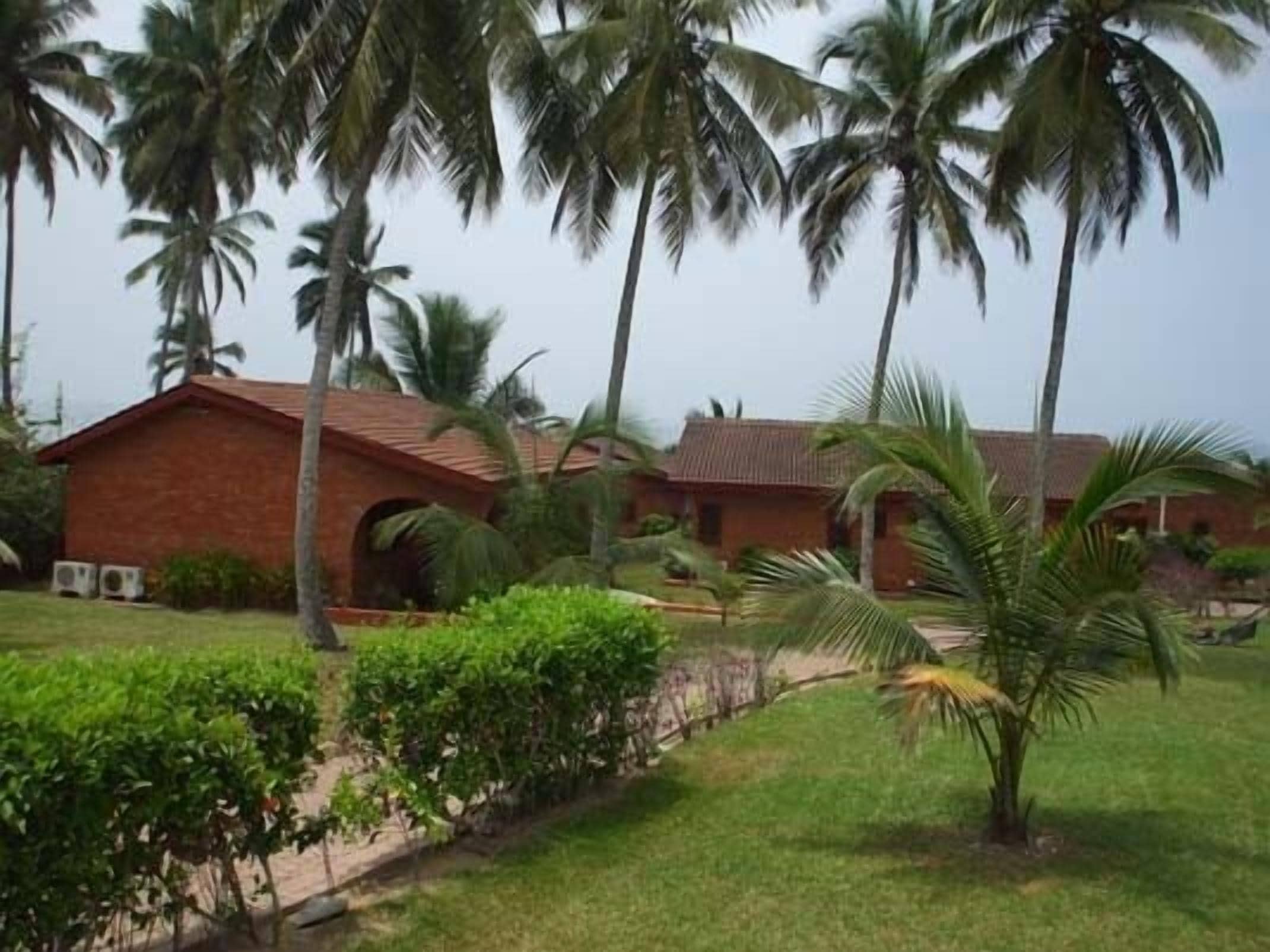 A brick building with a red roof, surrounded by palm trees and well-maintained greenery.