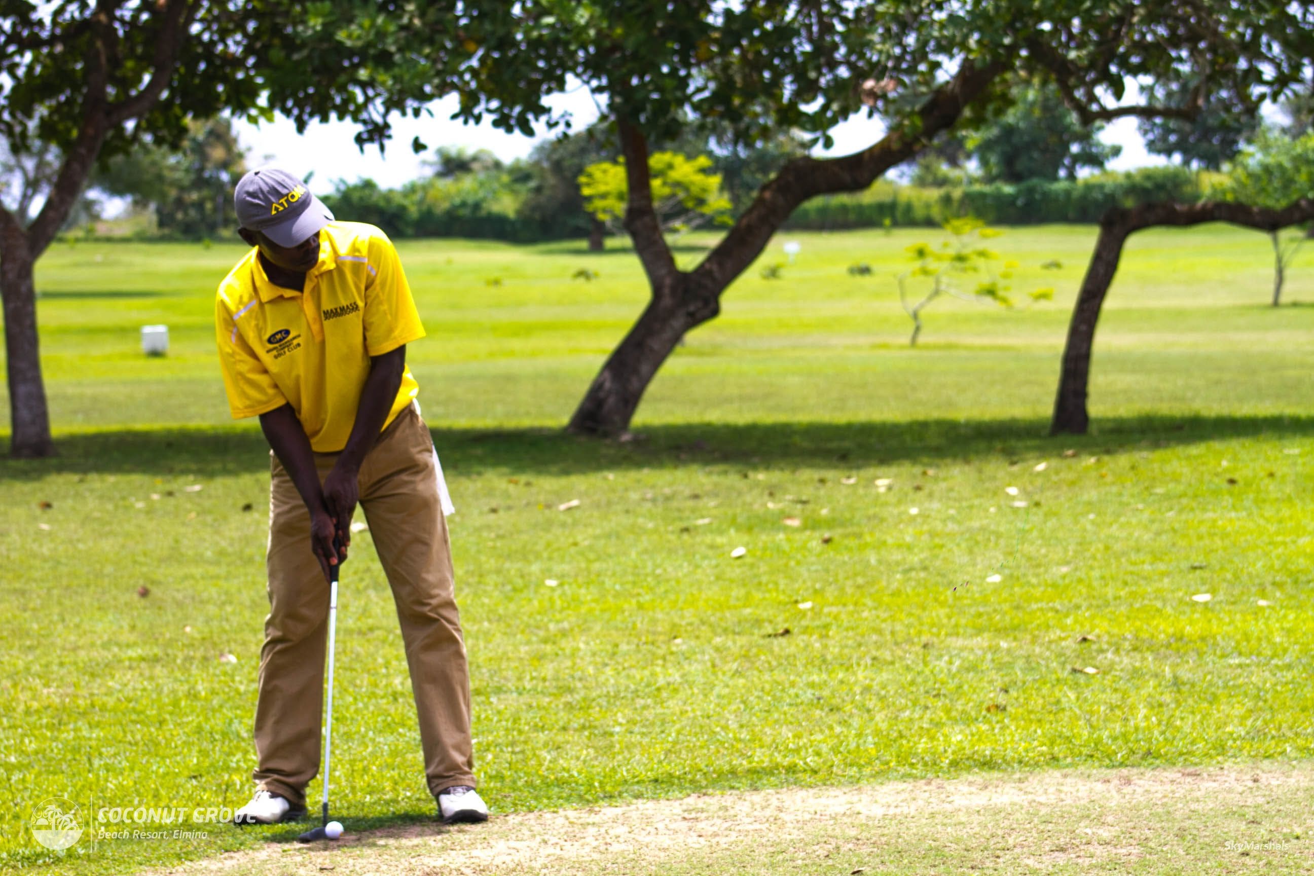 A golf course with a player in a yellow shirt and khaki pants preparing to putt.