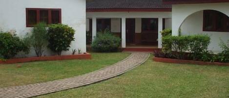 A courtyard with a paved walkway leading to a building with a tiled roof and a covered porch.
