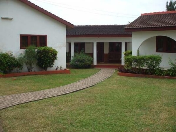 A courtyard with a paved walkway leading to a building with a tiled roof and a covered porch.