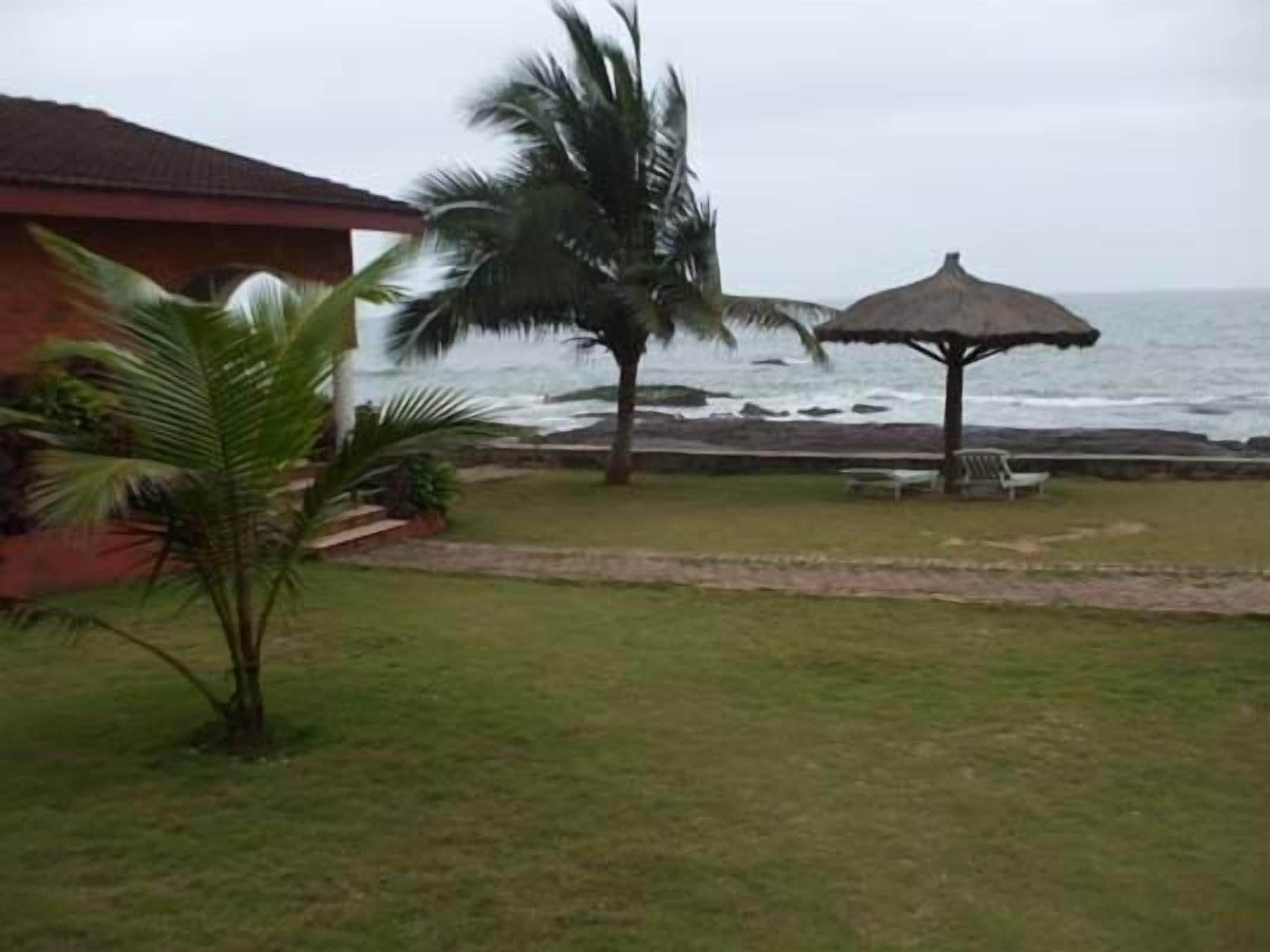 A beachside view with a thatched umbrella, palm trees, and a building with a red roof.