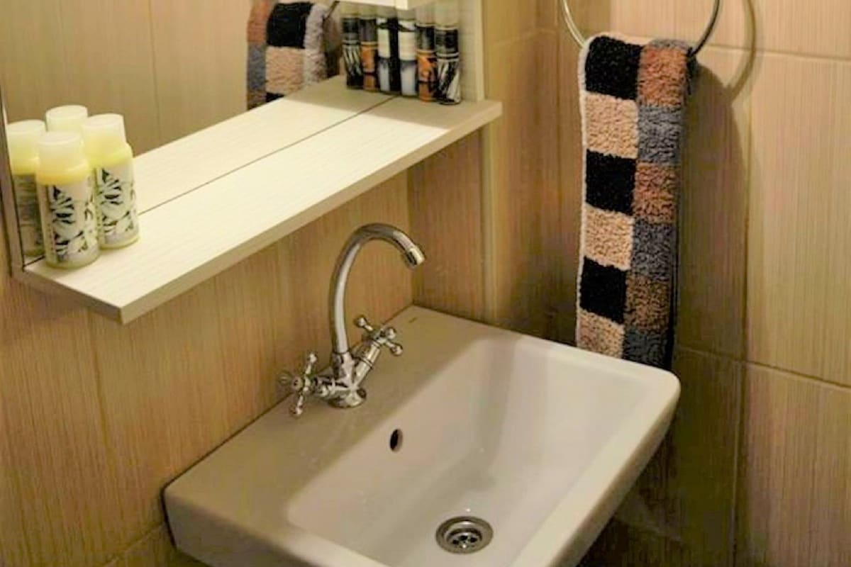 A bathroom with a sink, mirror, towel rack, and shelf with toiletries.