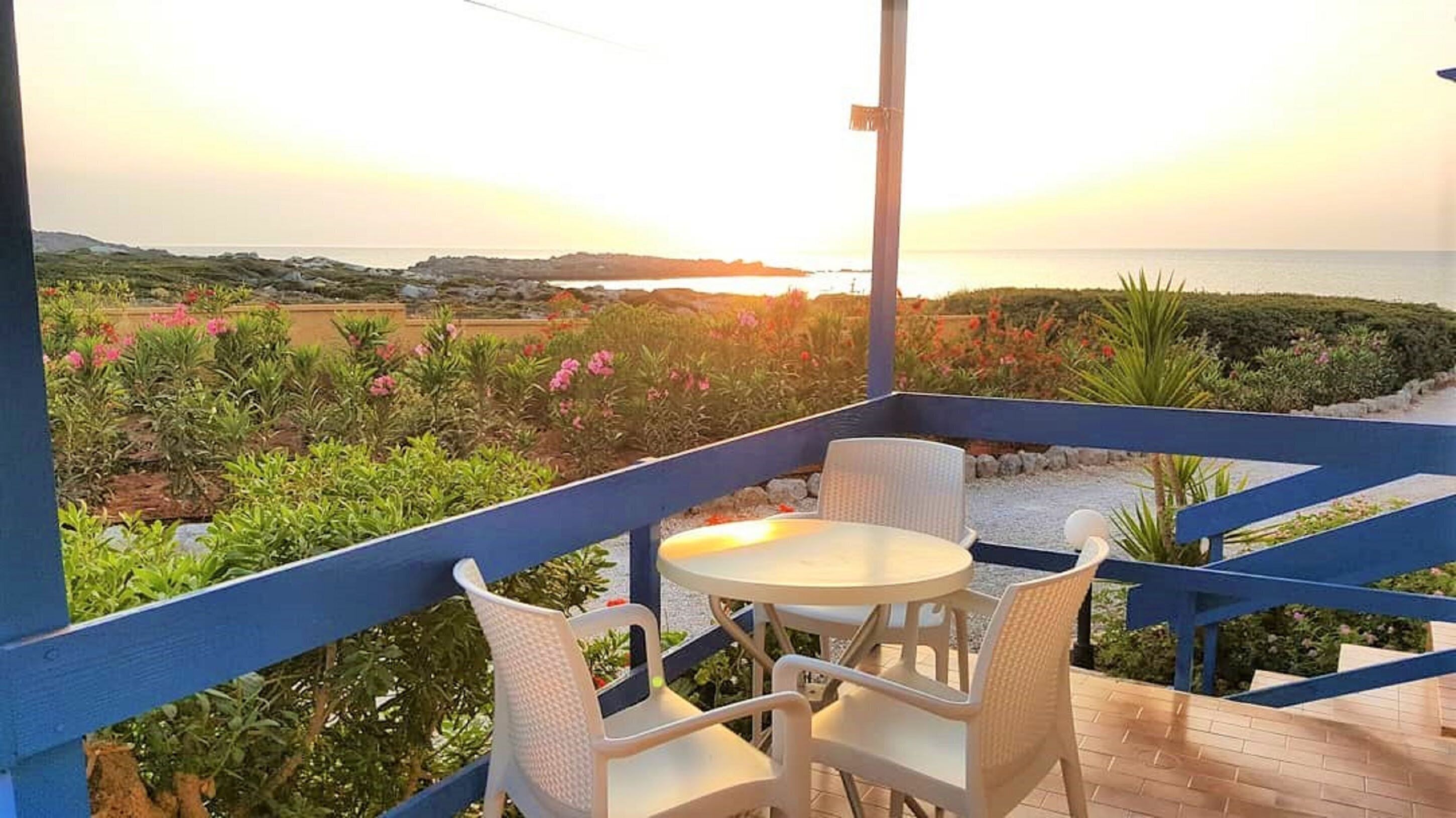 An outdoor seating area with a table and chairs, overlooking a coastal landscape with vegetation and a view of the sea.