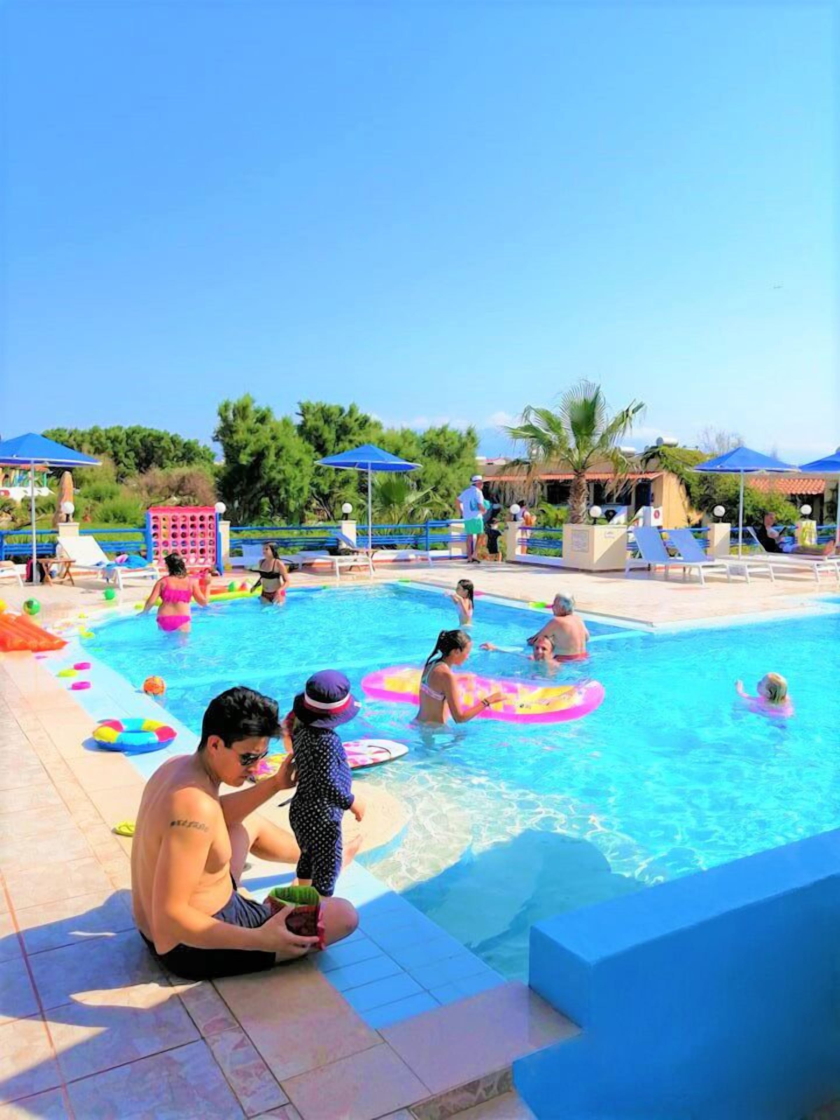 Zona de piscina con varias personas, incluyendo niños y adultos, disfrutando del agua.