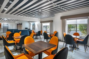 A modern dining area with black and white striped ceiling, orange and black chairs, and a view of the outdoors through large windows. - Comfort Inn Goshen (Goshen)