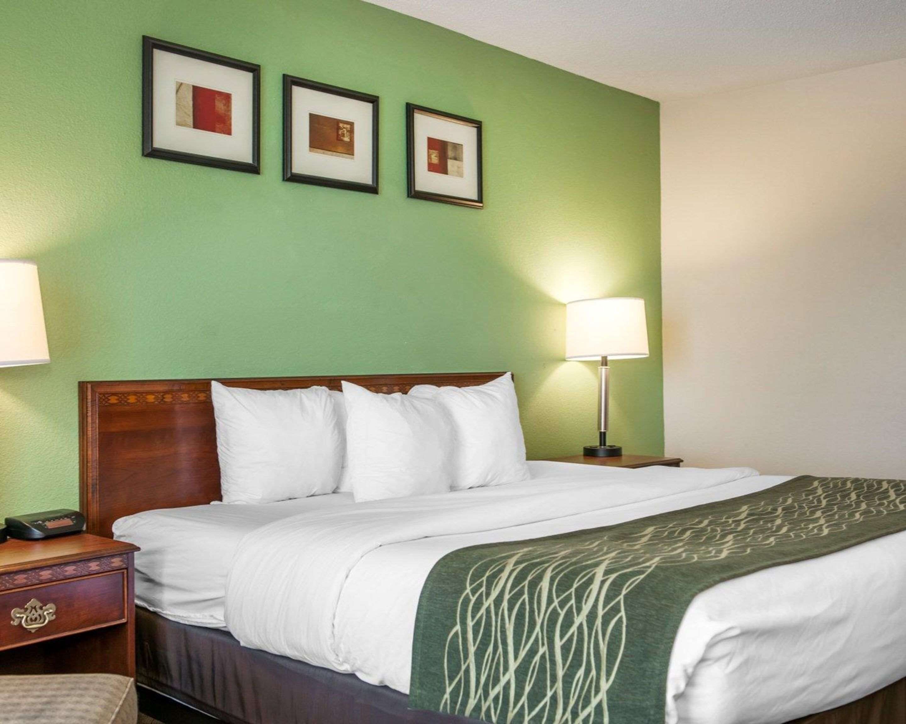 A hotel room with a bed, two bedside lamps, a nightstand, and three framed pictures on the wall.