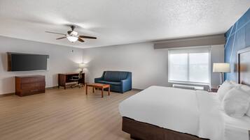 A hotel room with a bed, a desk, a chair, a ceiling fan, a TV, and a window.
