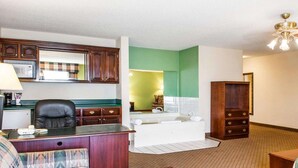 A compact living room with a sofa, a wooden coffee table, a desk with a chair, a kitchenette with a microwave, and a bathroom with a bathtub. - Comfort Inn Goshen (Goshen)