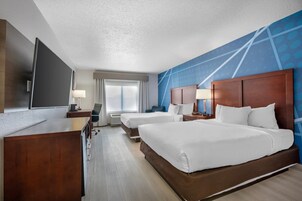 Habitación de hotel con una cama grande, un escritorio, un televisor y una ventana con cortinas.