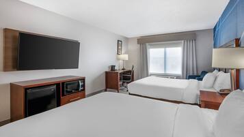 Quarto de hotel com duas camas, televisão de tela plana, escrivaninha com computador, abajur e janela com cortinas.