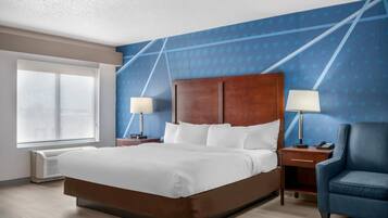 A hotel room with a large bed, two bedside tables with lamps, a chair, a large window, and a blue patterned wall.