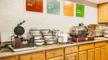 A breakfast bar with waffle makers, bowls, and a coffee station.