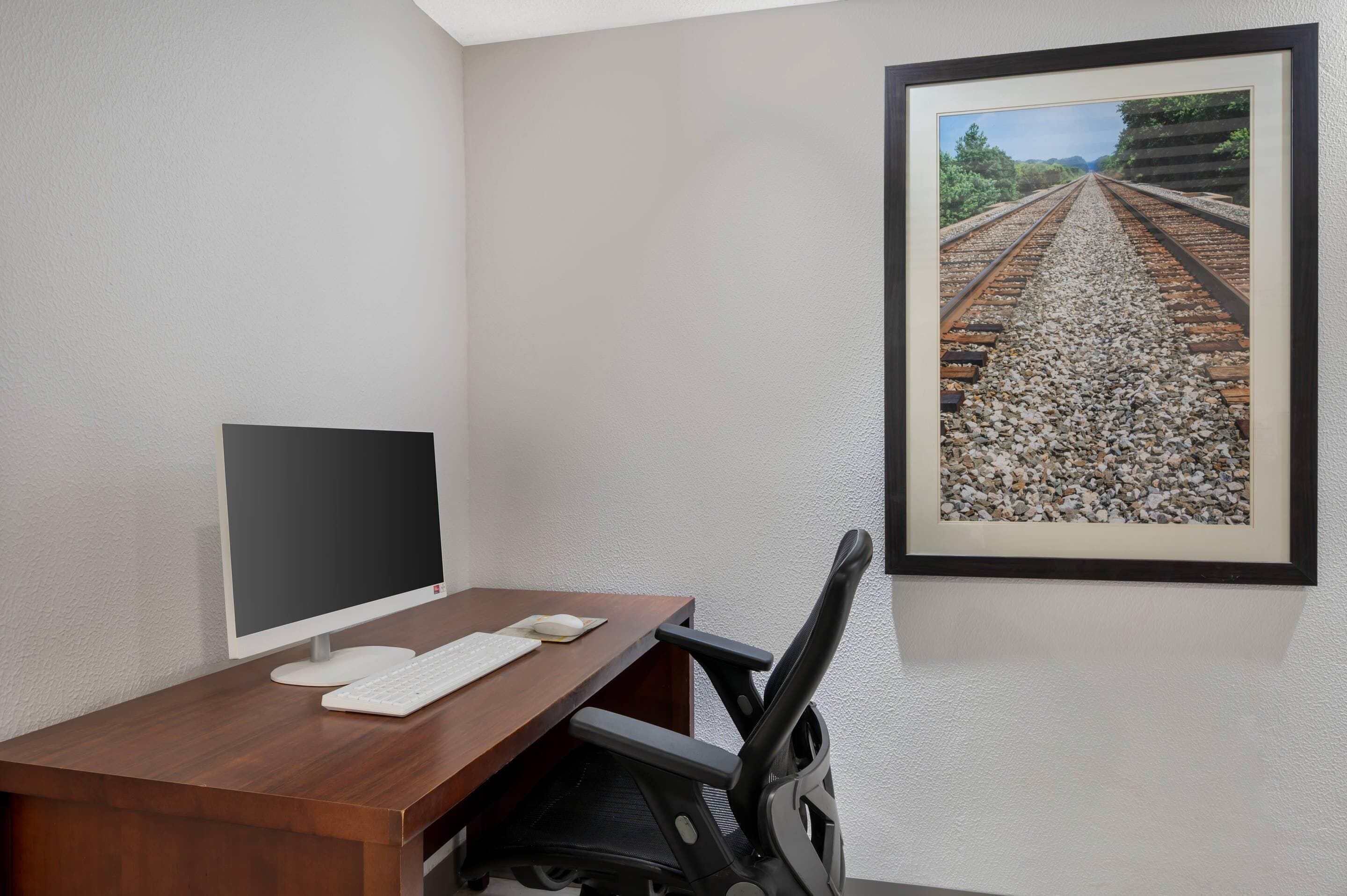 A workspace with a desk, computer, keyboard, mouse, and a framed picture of train tracks.