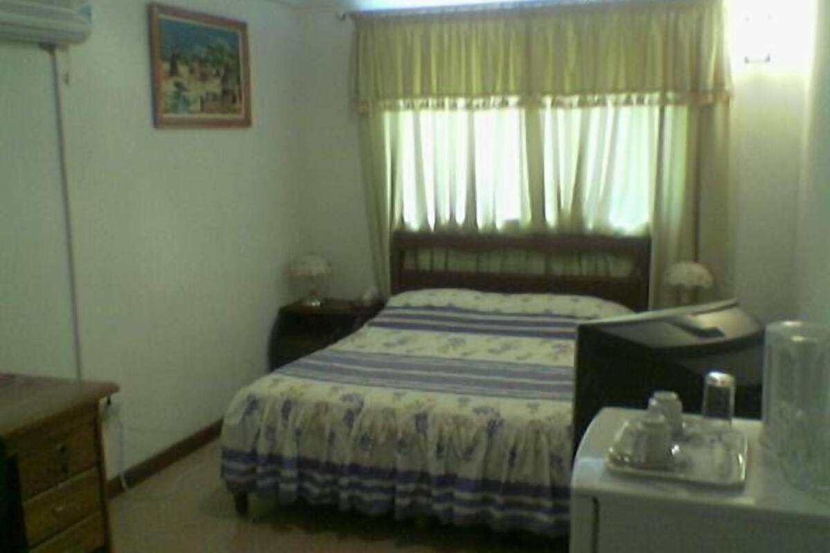 A hotel room with a bed, a nightstand, a lamp, and a window with curtains.