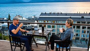 Two people seated at a table on a wooden deck with a view of a lake and mountains in the background.