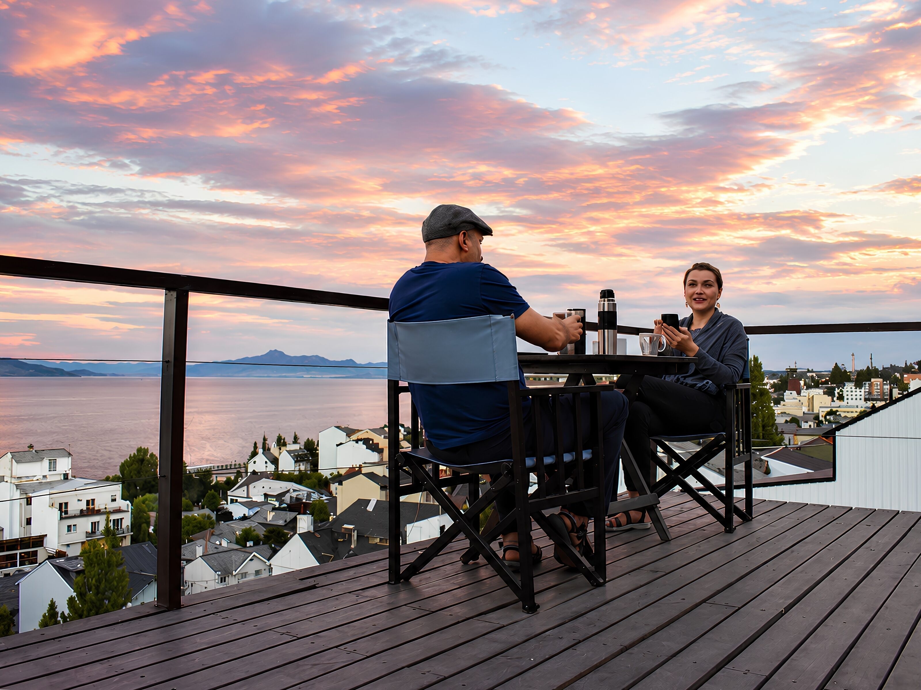 Una pareja sentada en una mesa con una vista panorámica de un cuerpo de agua y edificios al fondo.