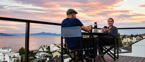 A couple seated at a table with a scenic view of a body of water and buildings in the background.