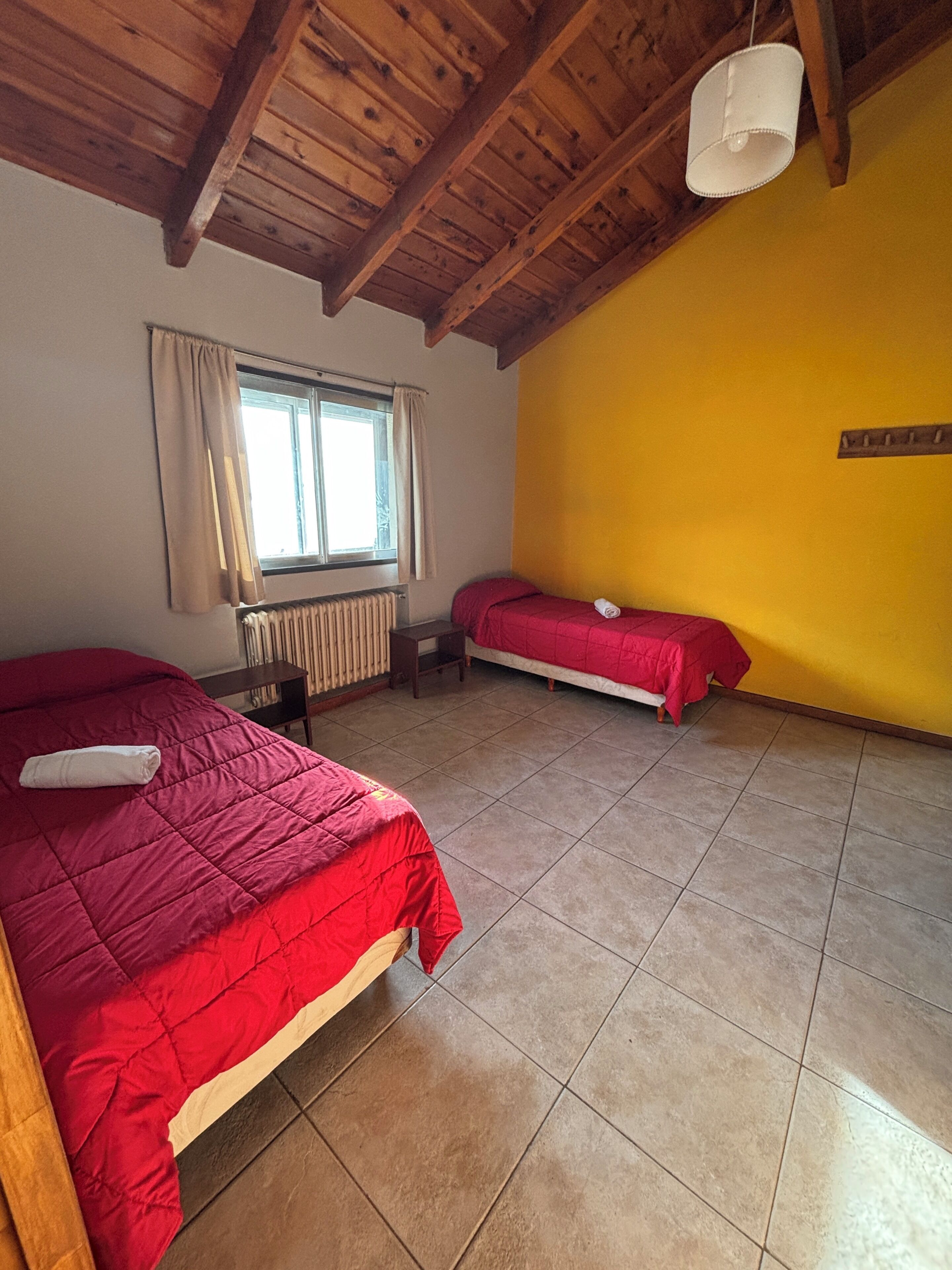 Una habitación con dos camas, una ventana con cortinas, un radiador y una pared amarilla.