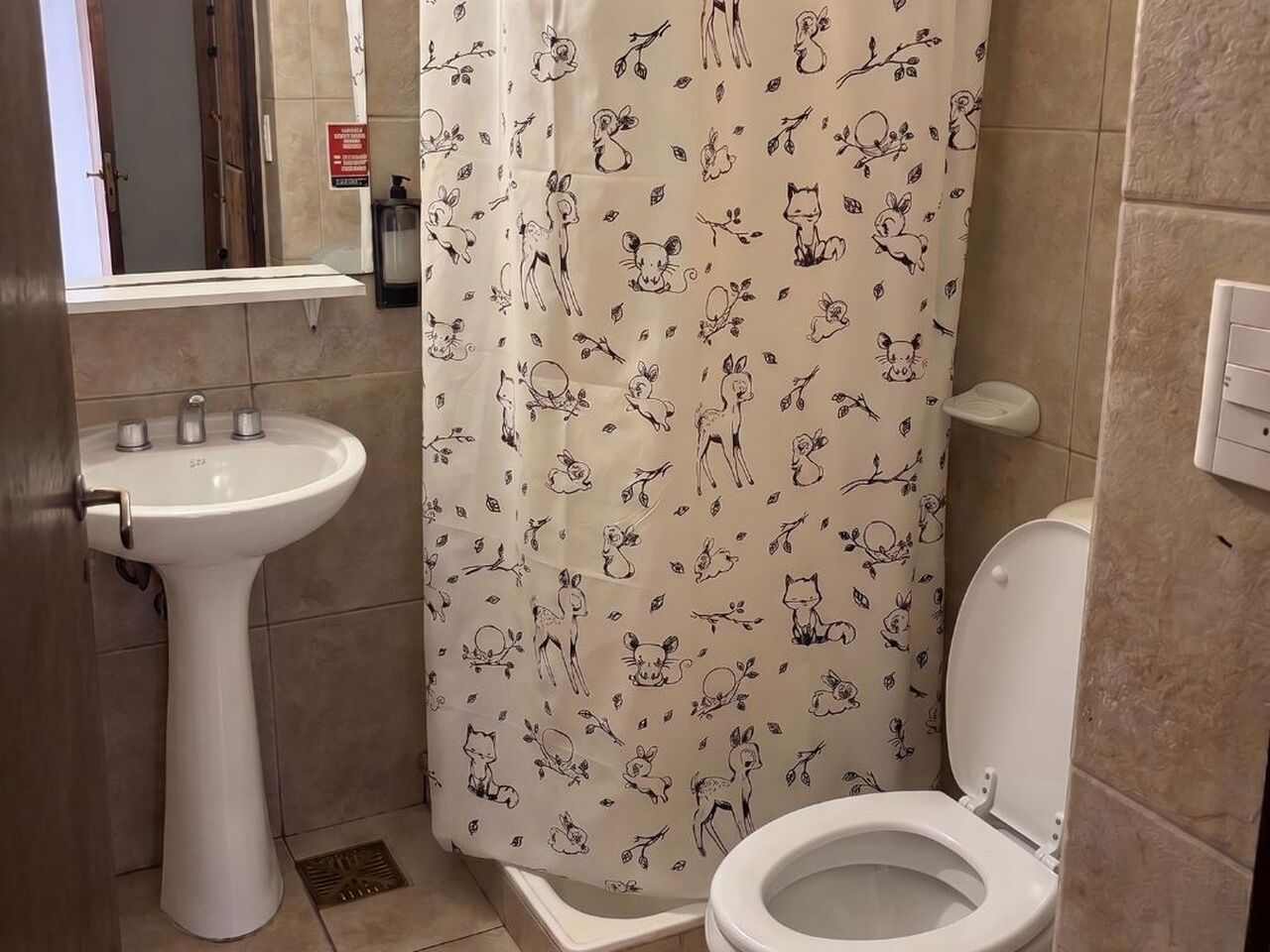 Un baño con un lavamanos pedestal blanco, un inodoro y una cortina de ducha con estampados de animales.