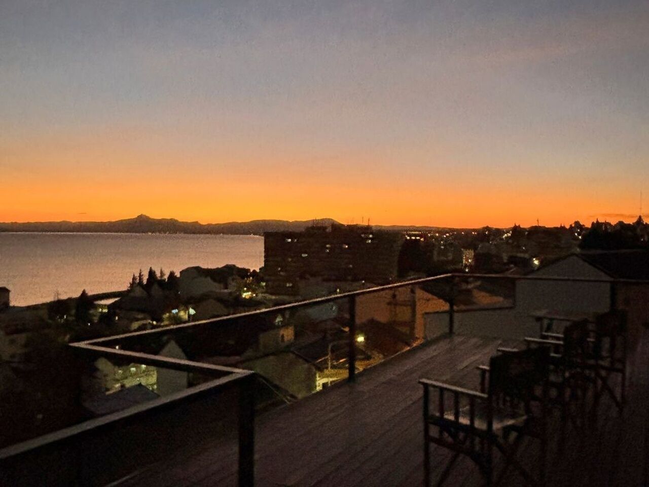 Terraza en la azotea con vista al mar y colinas lejanas al atardecer.