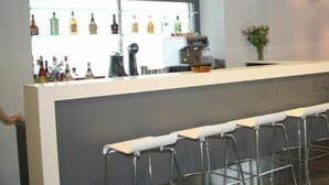 A bar area with a counter, bar stools, and a display of liquor bottles. - Hotel Des Roses (Kifisia)
