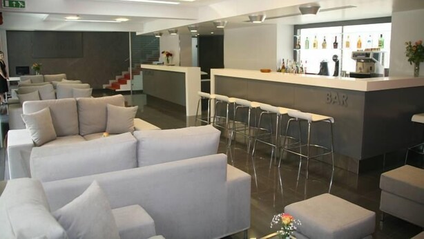 A modern lobby with a reception desk, bar area, and seating arrangement. - Hotel Des Roses (Kifisia)