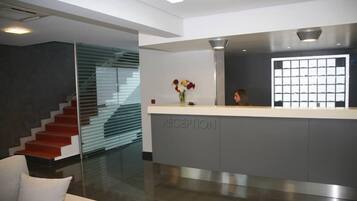 Zona de recepción con diseño moderno, que incluye un mostrador de recepción, una escalera y un panel de vidrio.