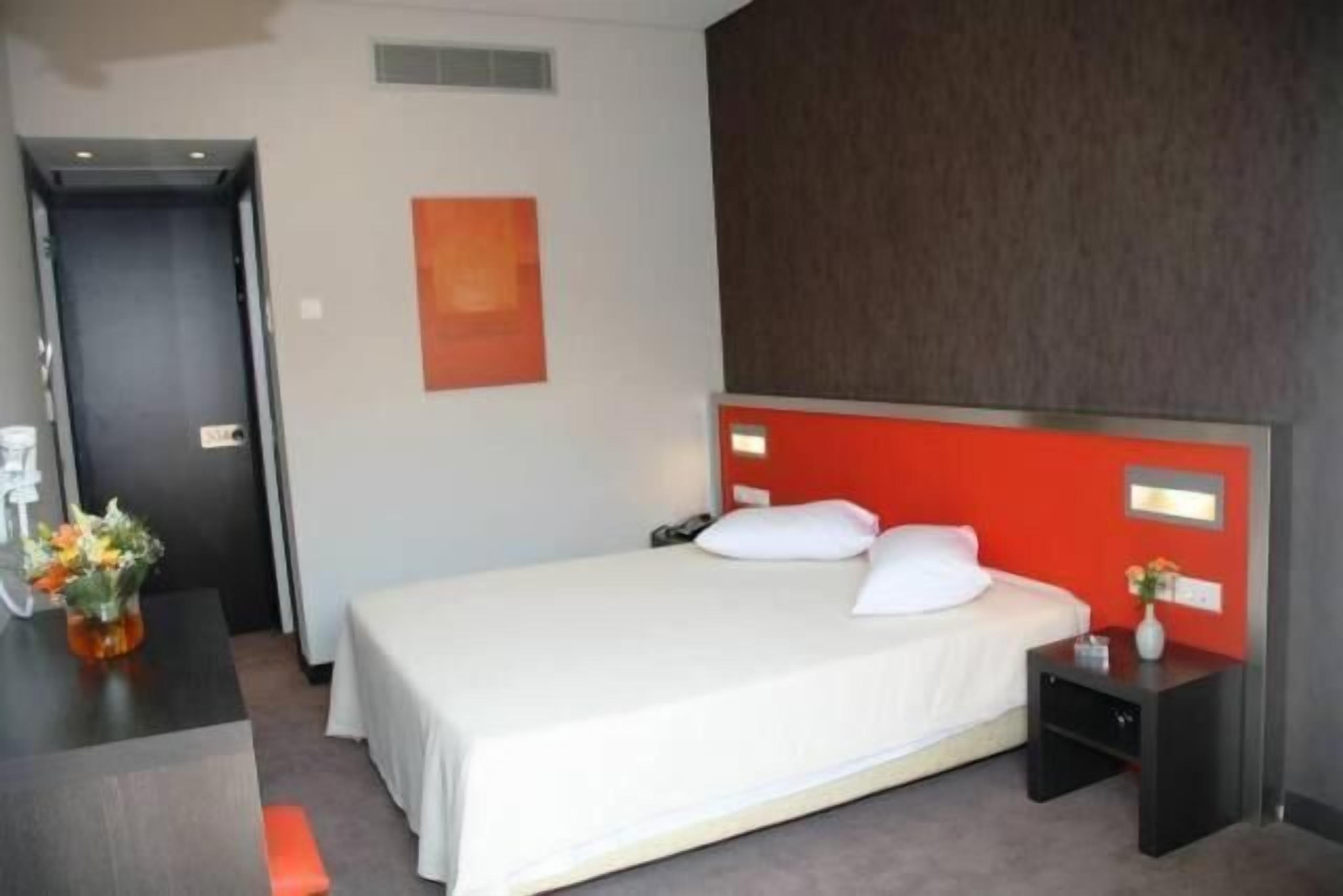 Une chambre d’hôtel avec un lit, un bureau et une chaise. Il y a une porte et un mur avec un panneau rouge.