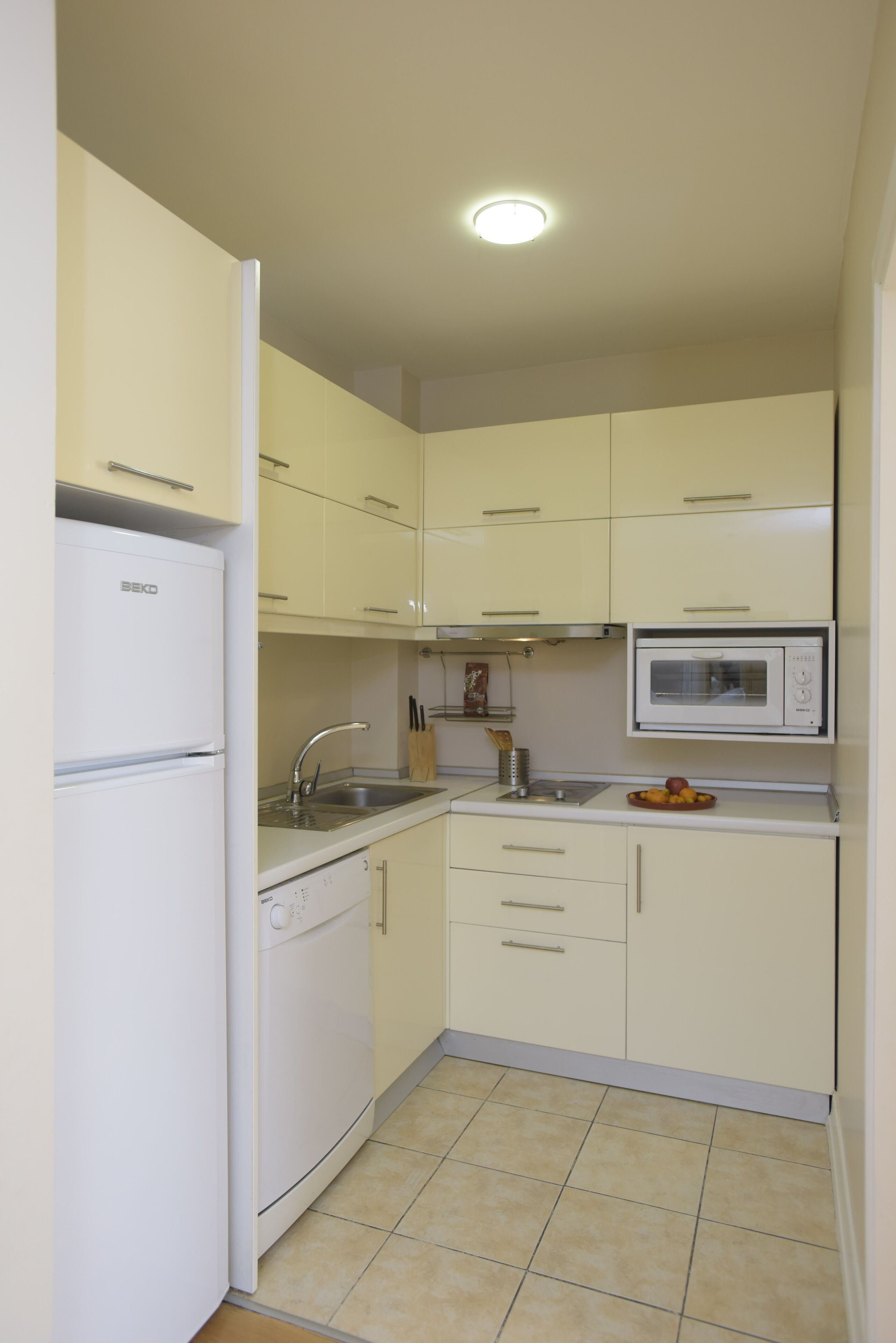 A compact kitchen with white cabinets, a built-in microwave, a dishwasher, and a sink.